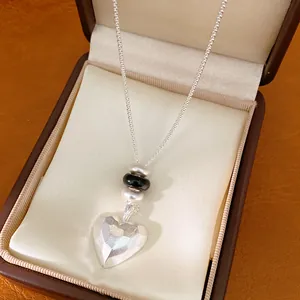 Gros plan élégant d'un collier pendentif cœur mat avec perles dans une boîte à bijoux marron.