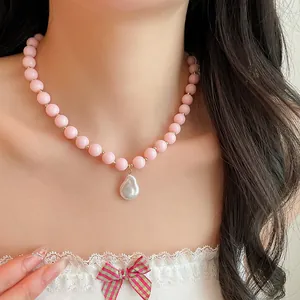 Detail shot of a pink acrylic bead necklace featuring a white baroque pearl pendant on model