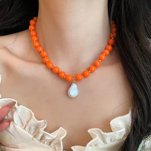 Close-up of vibrant orange acrylic bead necklace with a white baroque pearl pendant.
