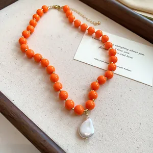 Close-up detail of a vibrant orange acrylic bead necklace with white baroque pearl pendant