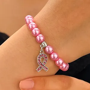 Detail showing a pink ribbon rhinestone charm on a pink faux pearl bracelet worn on a wrist.