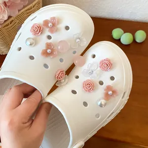 Detail view of resin flower shoe charms with pink roses and pearls on white clogs.