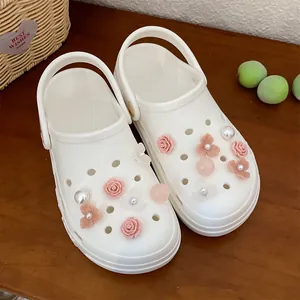 Detailed close-up of pink resin flower and pearl shoe charms on stylish white clogs
