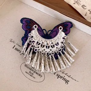 Dettaglio di fermaglio etnico con farfalla ricamata viola e nappe metalliche argentate