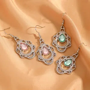 Close-up van vintage Boheemse hol gegraveerde druppeloorbellen met roze en groene stenen.