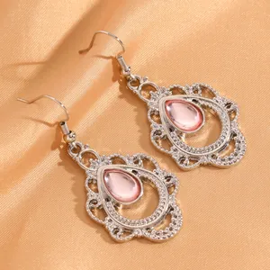 Close-up van bohemian zilveren druppeloorbellen met roze stenen op goudkleurige zijden stof