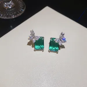 Primo piano di eleganti orecchini rettangolari verde smeraldo con dettaglio a farfalla.