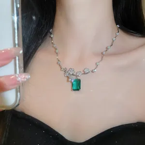 Dettaglio di una collana con pendente smeraldo e fiori di cristallo indossata da modella.