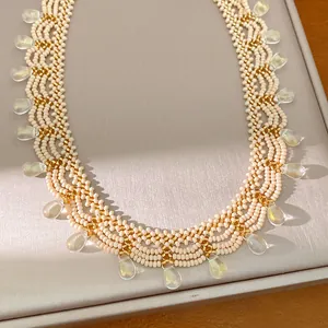 Macro detail of a vintage cream glass beaded lace necklace with gold accents and teardrop charms.