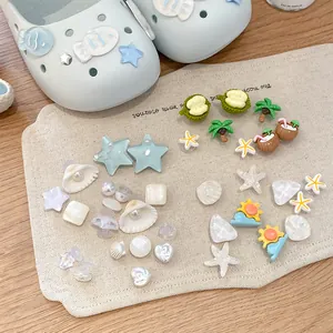 Dettaglio ciondoli estivi per scarpe con conchiglie, perle e motivi tropicali su tela.