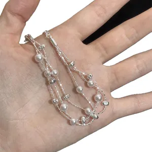Eleganter mehrlagiger Armreif mit weißen Perlen und Silberperlen an der Hand gezeigt