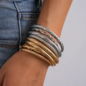 Close-up van gestapelde goud- en zilverkleurige metalen armbanden om een pols met denim