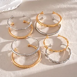 Diverse goud- en zilverkleurige C-vormige armbanden met getordeerde en gehamerde texturen.