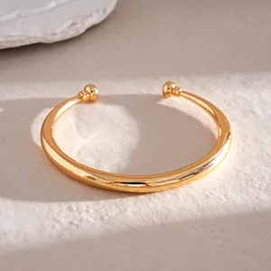 Close-up van een minimalistische goudkleurige C-vormige open armband op een stenen vlak.
