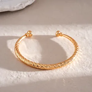 Detailweergave van een goudkleurige C-vormige armband met elegante gedraaide textuur