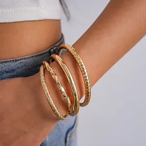 Detail van gelaagde gouden geometrische armbanden met diverse texturen