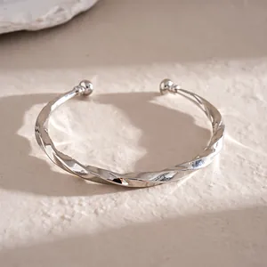 Detailopname van een zilveren gedraaide C-vormige open metalen armband sieraad