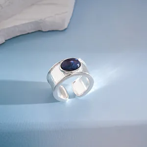 Vista detallada de un anillo ancho de plata con una piedra de resina azul y metal cepillado.