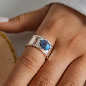 Primer plano de un anillo ancho plateado con incrustación de resina azul en un dedo