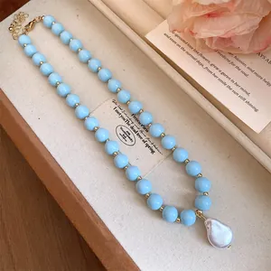 Detailed view of a light blue beaded necklace with a large baroque pearl pendant on a tray.