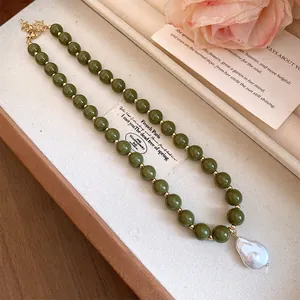 Detail view of a vintage green bead necklace with a baroque pearl pendant in a box.