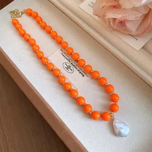 Close-up of orange acrylic beads and a white baroque pearl pendant necklace in a gift box