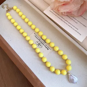 Detailed view of yellow acrylic bead necklace with baroque pearl pendant in a jewelry box