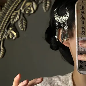 Gros plan d'une pince à cheveux argentée en forme de lune avec des glands en métal