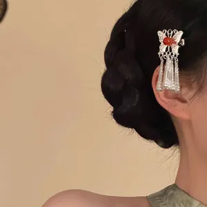 Détail d'une pince à cheveux papillon argentée avec perles rouges et pompons sur tresse