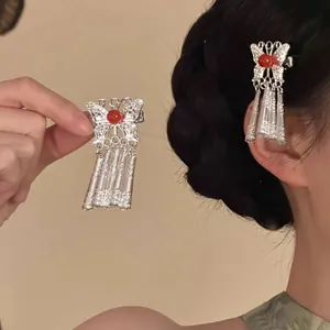 Vue détaillée d'une pince à cheveux papillon en métal avec perle rouge et pompons.