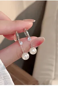 Close-up of elegant pearl drop earrings with zircon studs on silver hoops.