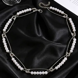 Primer plano de collar gargantilla punk con imperdibles y perlas sobre tela de satén negro