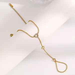 Détail d'un bracelet de doigt en acier inoxydable doré avec un charm en forme de cœur.