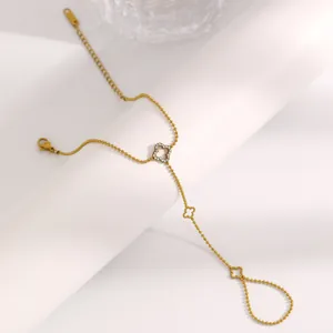 Détail d'un bracelet de doigt en acier inoxydable doré avec un motif trèfle scintillant.