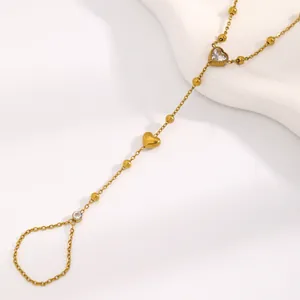 Détail d'un bracelet de doigt en acier inoxydable doré avec cœur et chaîne à billes.