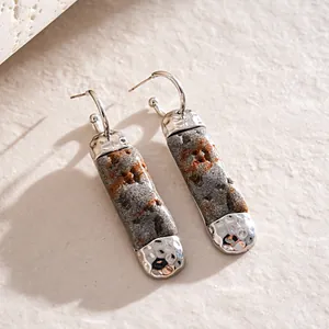Close-up of distressed stone-like resin earrings with hammered silver-tone metal details.