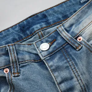 Gros plan d'un jean slim montrant le délavage du tissu et les garnitures métalliques