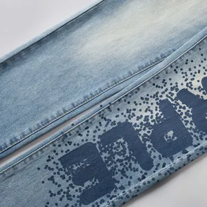 Détail d'un jean en denim bleu clair avec éclaboussures d'encre bleue et lettres