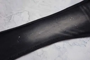 Détail gros plan d'un jean évasé noir avec des éclaboussures de peinture blanche et texture usée.