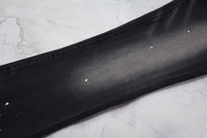 Détail de près d'un jean évasé noir pour homme avec des taches de peinture blanche.