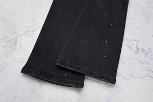 Détail du bas d'un jean évasé noir avec des finitions de taches de peinture blanche
