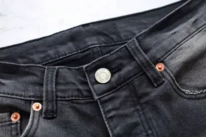 Gros plan sur le bouton métallique gravé et les rivets d'un jean évasé noir pour homme
