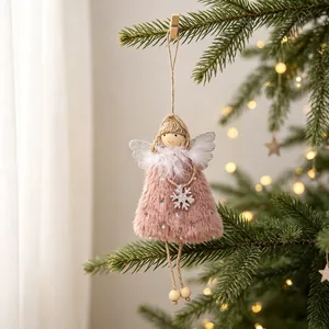 Close-up of a pink fuzzy Christmas angel doll hanging on a pine tree with warm lights