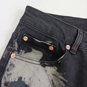 Dettaglio dei rivetti in rame vintage e del lavaggio grigio su jeans in denim nero da uomo