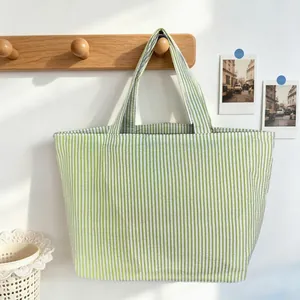 Detail of a green striped tote bag hanging on a minimalist wooden wall hook