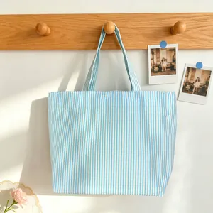 Detail of a blue and white striped tote bag hanging on a wooden hook in a cozy setting.