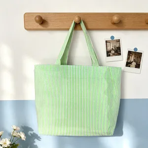 Detailed view of a green and white striped seersucker tote bag hanging on a wooden hook