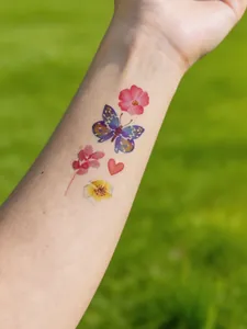 Close-up of colorful watercolor butterfly and flower temporary tattoos on person's forearm.