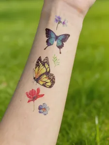 Detail view of colorful watercolor butterfly and flower temporary tattoos on arm