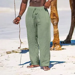 Detail of sage green breathable cotton linen loose fit men's trousers on a beach